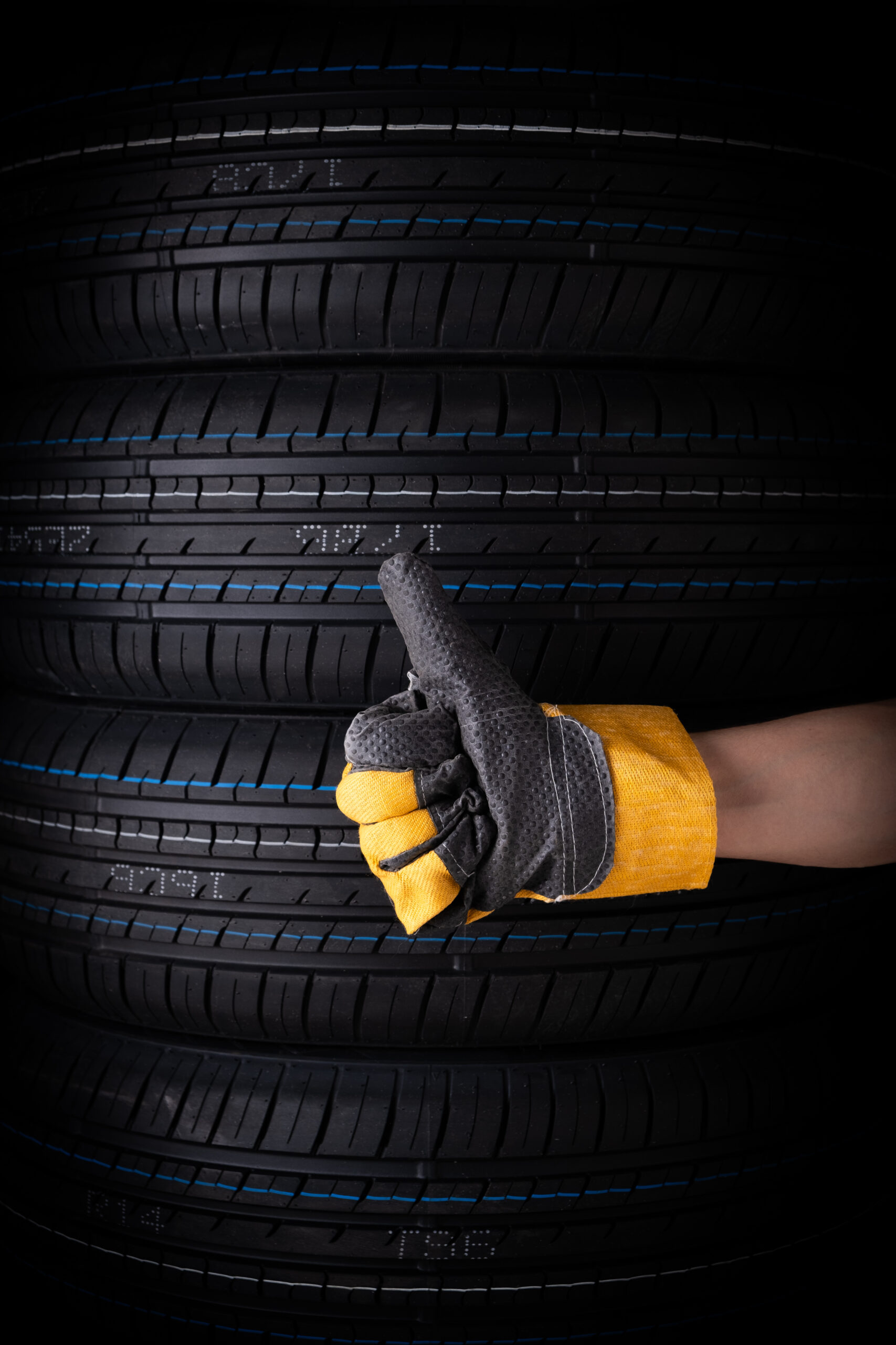 Hand in yellow gloves and car tires on black background, closeup